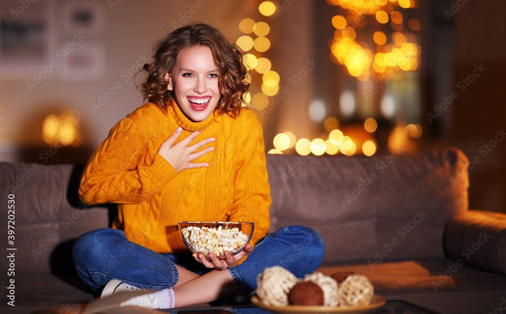 年轻快乐快乐的女人拿着爆米花在家里笑着看电视上的圣诞电影