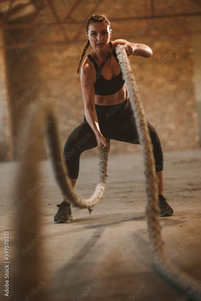 坚韧的女人在旧仓库里用战斗绳锻炼