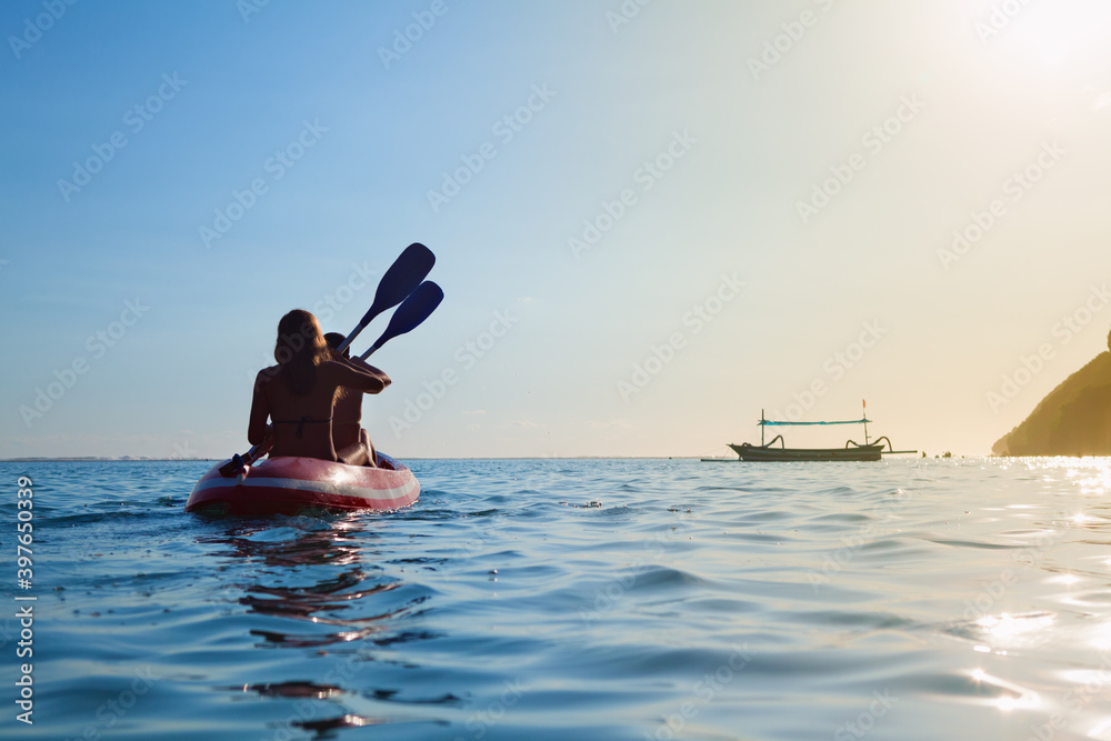 年轻女性在划船时玩得很开心。女孩们在泻湖边的皮划艇上划水。旅行生活方式，娱乐