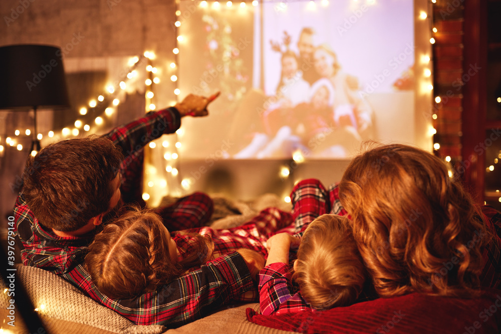 家庭母亲父亲和孩子在圣诞节晚上用爆米花看投影仪、电影、电影
