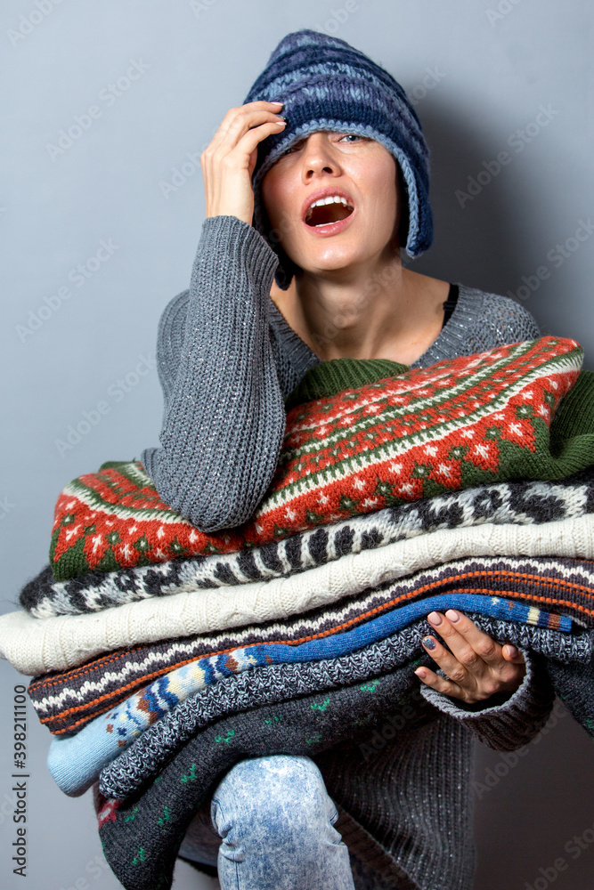 年轻女人拿着一堆毛衣，戴着针织帽，穿着灰色的保暖羊毛毛衣