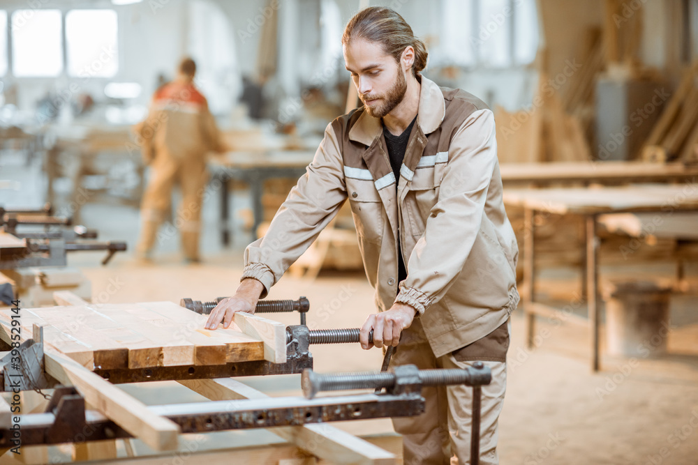 在木工制造过程中，穿着统一制服的英俊木匠用手压在木棒上。