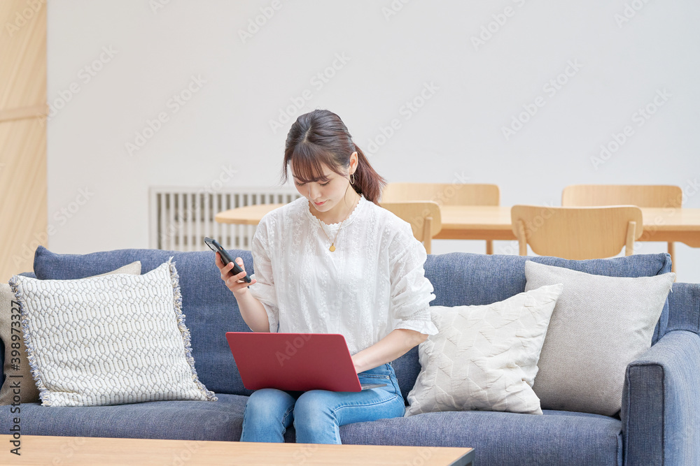 ソファーでスマホとパソコンを使う女性