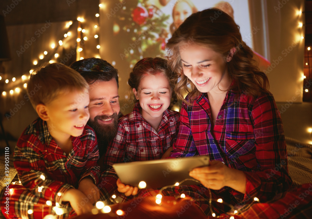 圣诞快乐！戴着发光花环的幸福家庭在圣诞假期的n床上进行视频通话