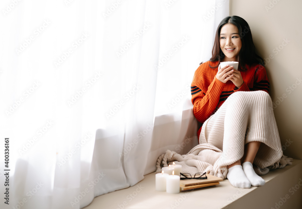 穿着针织保暖毛衣的年轻美丽的快乐亚洲女性坐在风边的椅子上