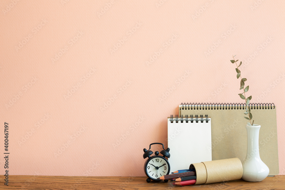 笔记本、时钟、铅笔，木桌上有桉树花瓶。粉色背景。工作和学习pl