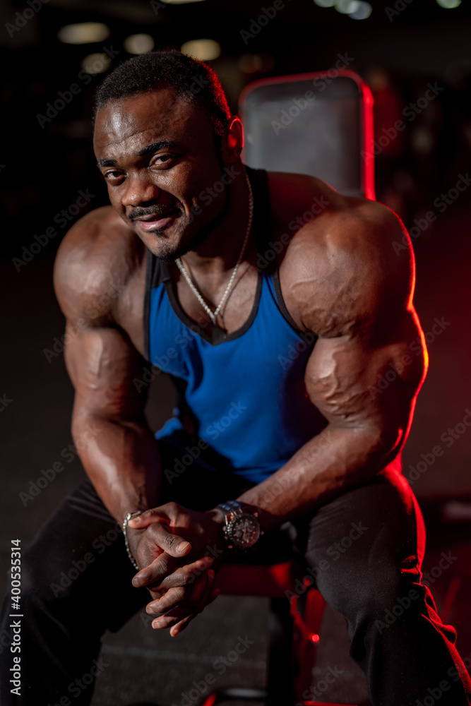 黑人男子在健身房里摆姿势。短发模特，肌肉发达，在黑暗的背景下看着镜头