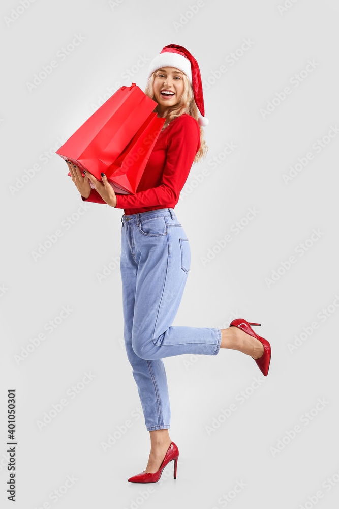 戴圣诞老人帽的漂亮年轻女子，浅色背景带购物袋
