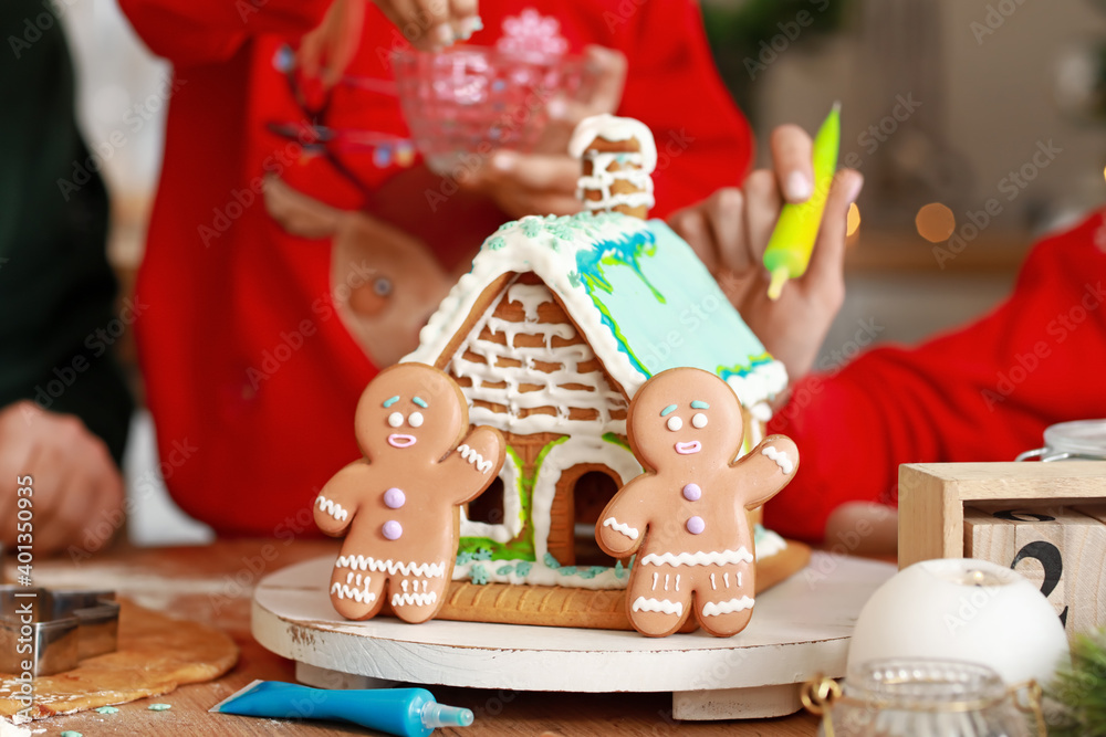 Family making tasty gingerbread house in kitchen on Christmas eve