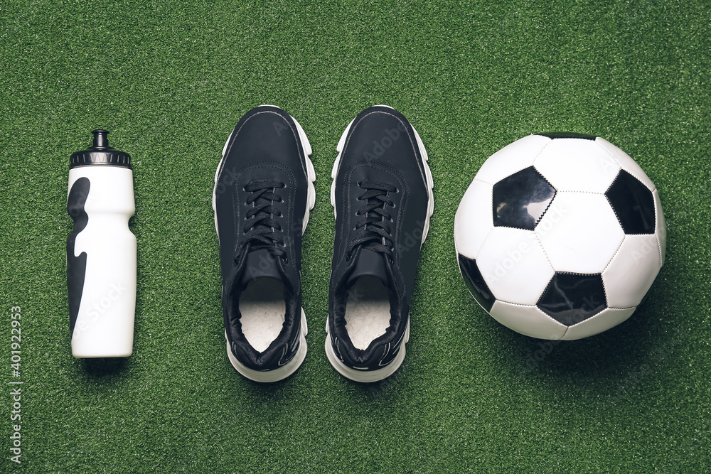 Sportive shoes, soccer ball and bottle of water on color background