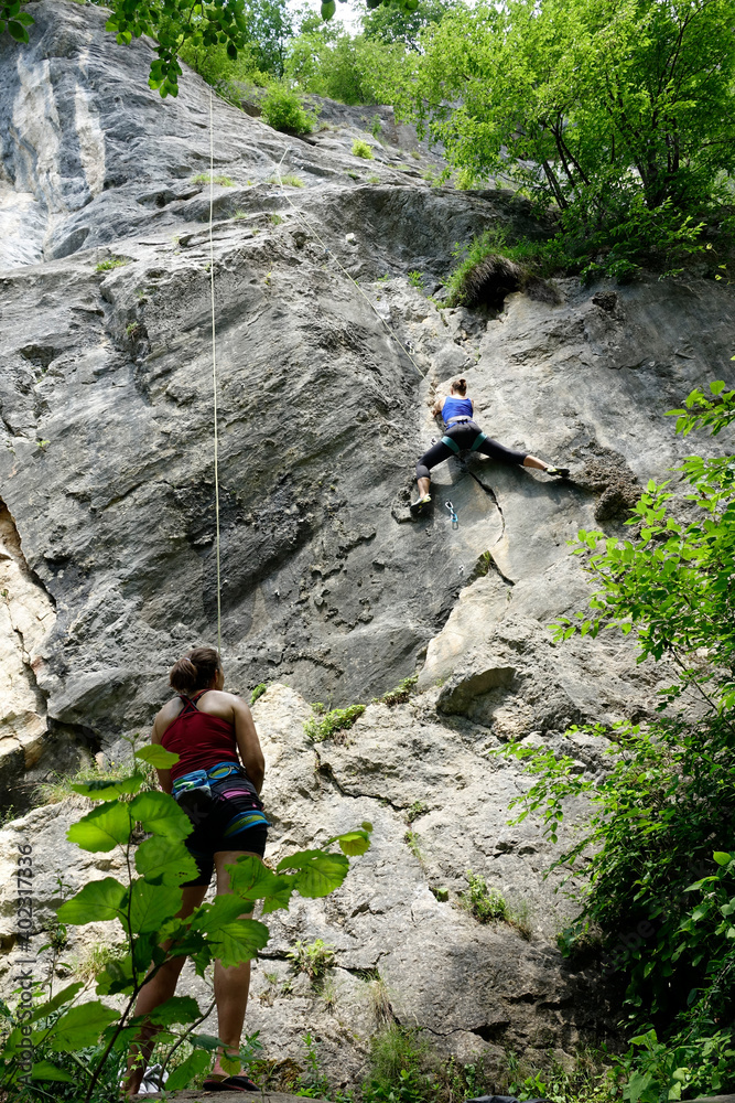 低角度：Belayer在照顾爬上高耸悬崖的健康女性登山者。