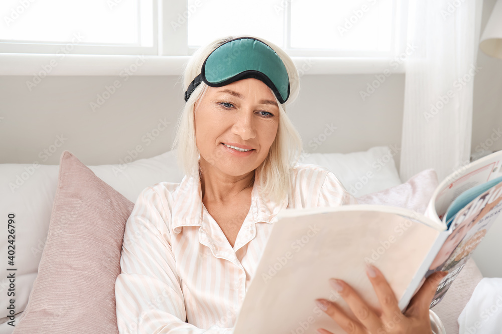 Mature woman reading magazine in bedroom