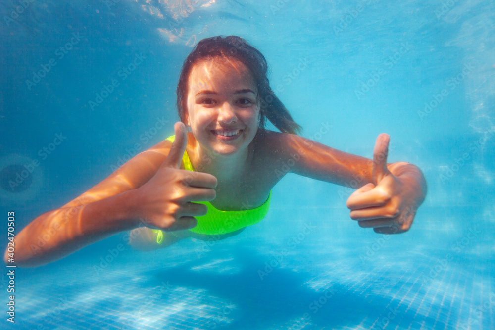 快乐微笑的少女，大拇指向上，笑容满面，在游泳池水下游泳