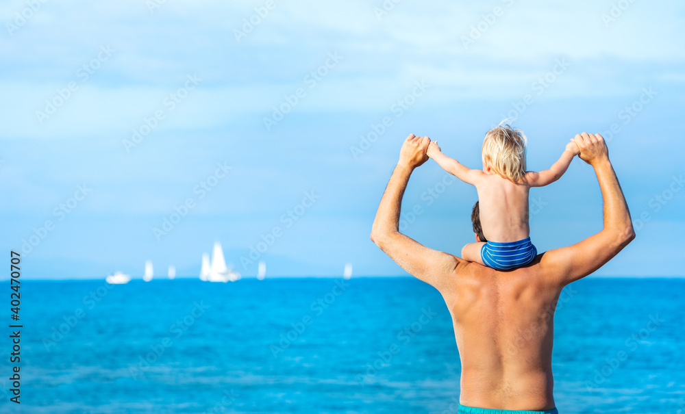 Father hold little toddler blond boy sitting on his shoulders and look at the sea with ships