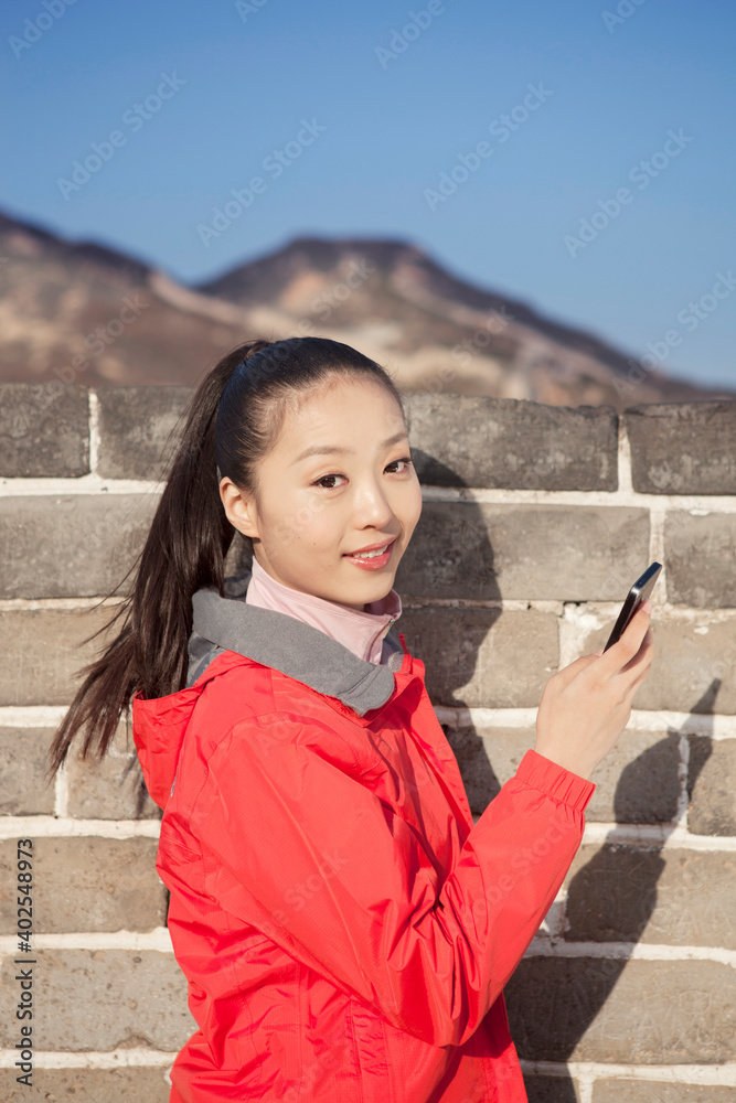 一名年轻女子在长城旅游中使用手机