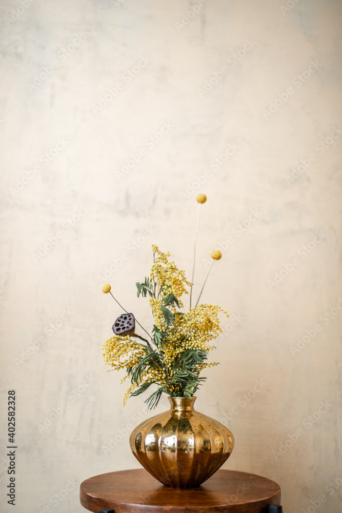 米色墙壁背景上的金色花瓶中的鲜花和香草的成分。Acacia的气味，