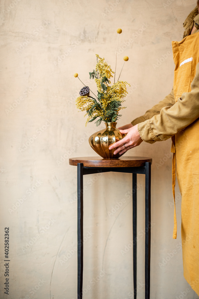 女性装饰家居，米色墙壁上的金色花瓶中有鲜花和香草