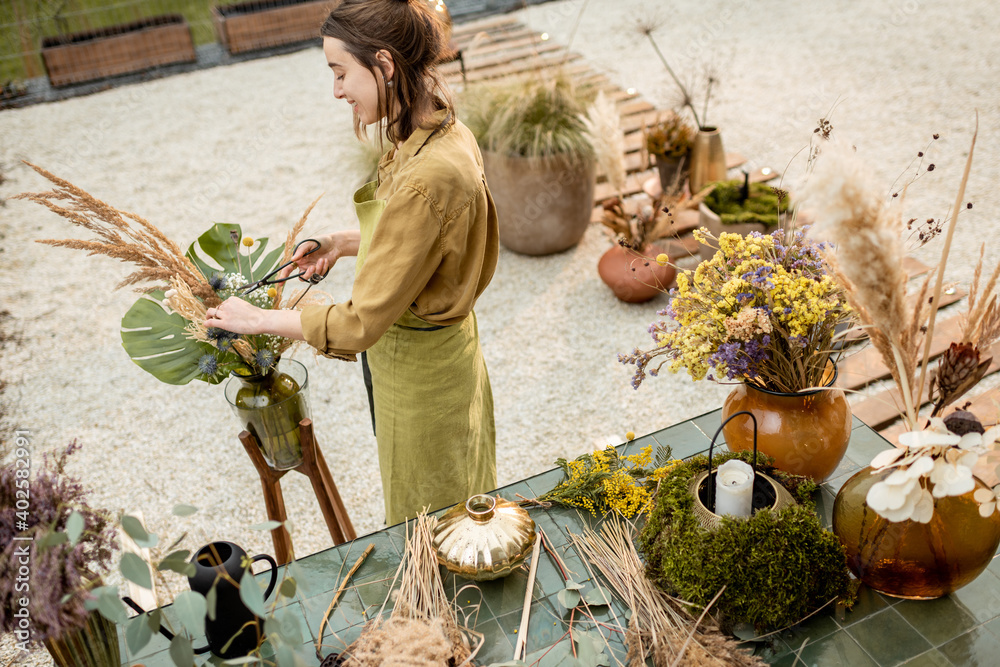 Young woman making compositions of dried and fresh flowers and herbs at the workshop outdoors. Flori