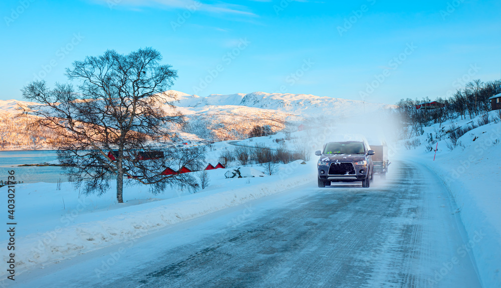 SUV行驶在冬季森林道路上-一辆汽车行驶在树木和雪山之间的积雪道路上-特罗姆瑟