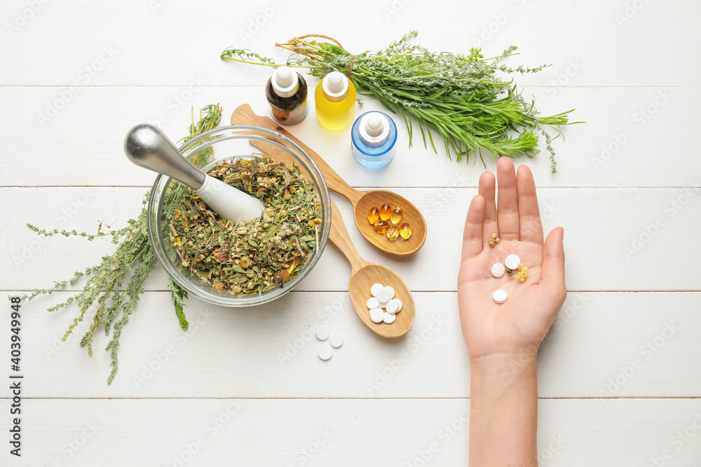 Female hand with pills, herbs and bottles of essential oil on light background