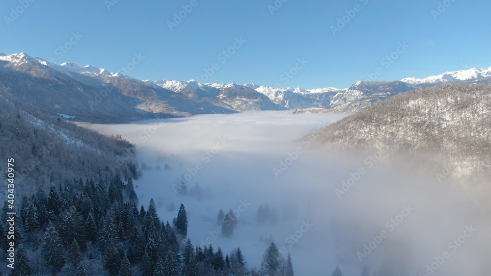 无人机：浓雾笼罩着壮观的雪山山脉下的山谷。