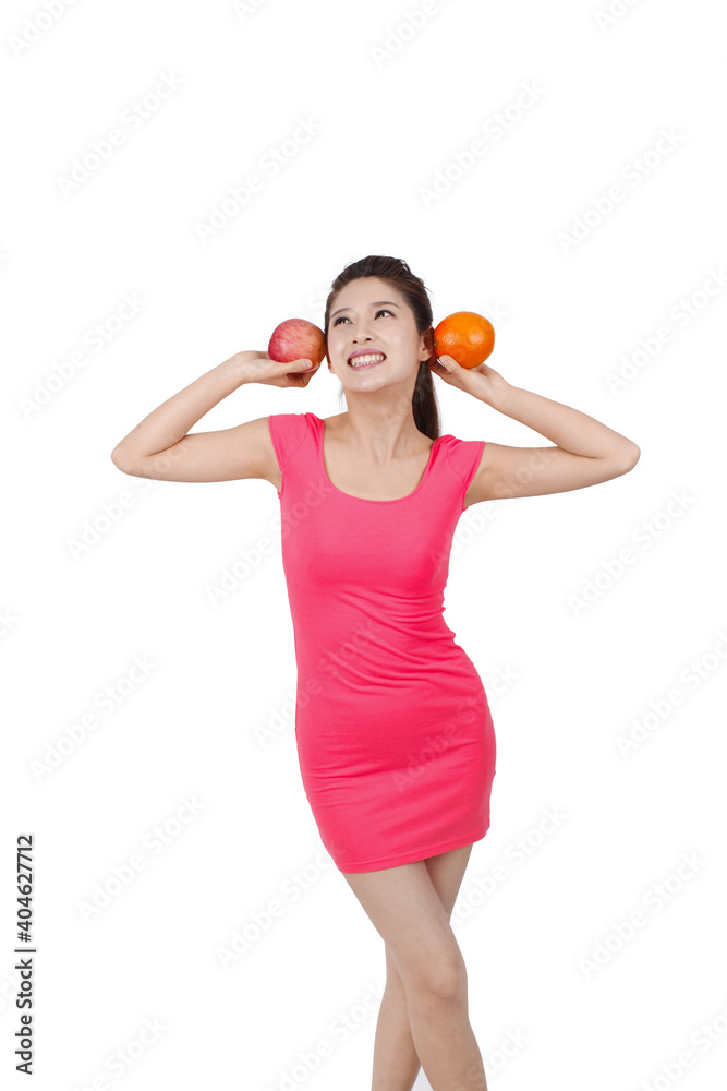 身穿粉色连衣裙的年轻女子手持苹果和橙色