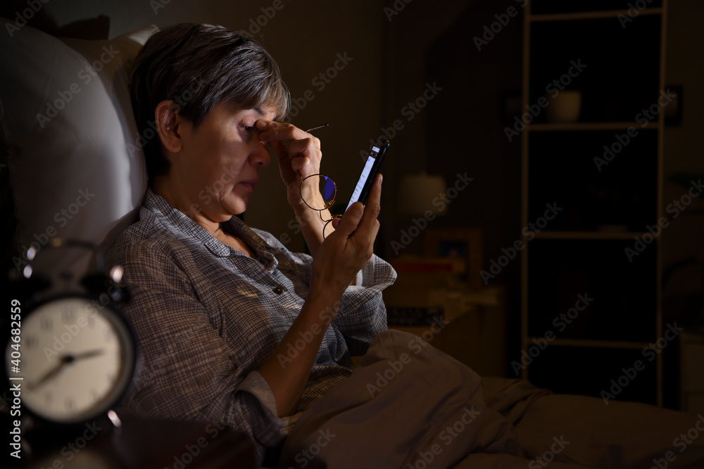 亚洲老年女性晚上躺在床上使用智能手机时眼睛酸痛