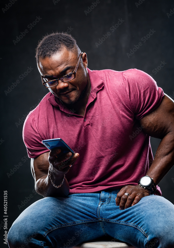 Smiling cheerful young black man poses with phone in hands over black background. African american i