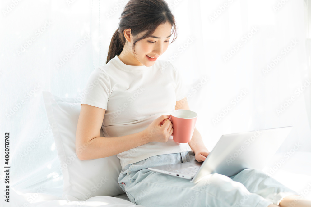 坐在床上工作的年轻亚洲女性观看家庭娱乐节目
