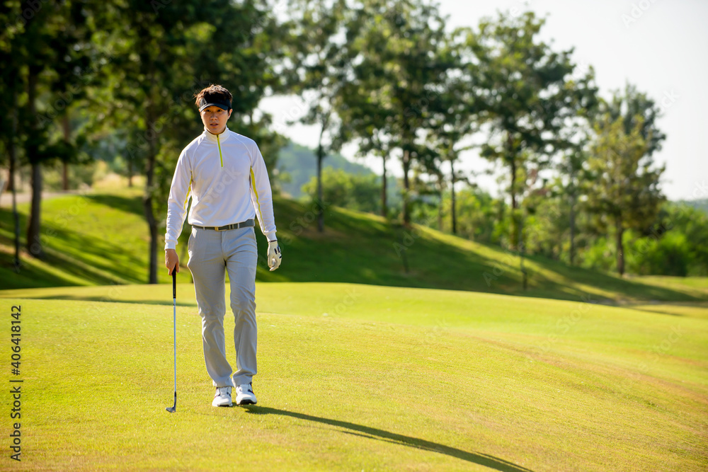 亚洲男子高尔夫球手手持高尔夫球杆在高尔夫球场球道上行走