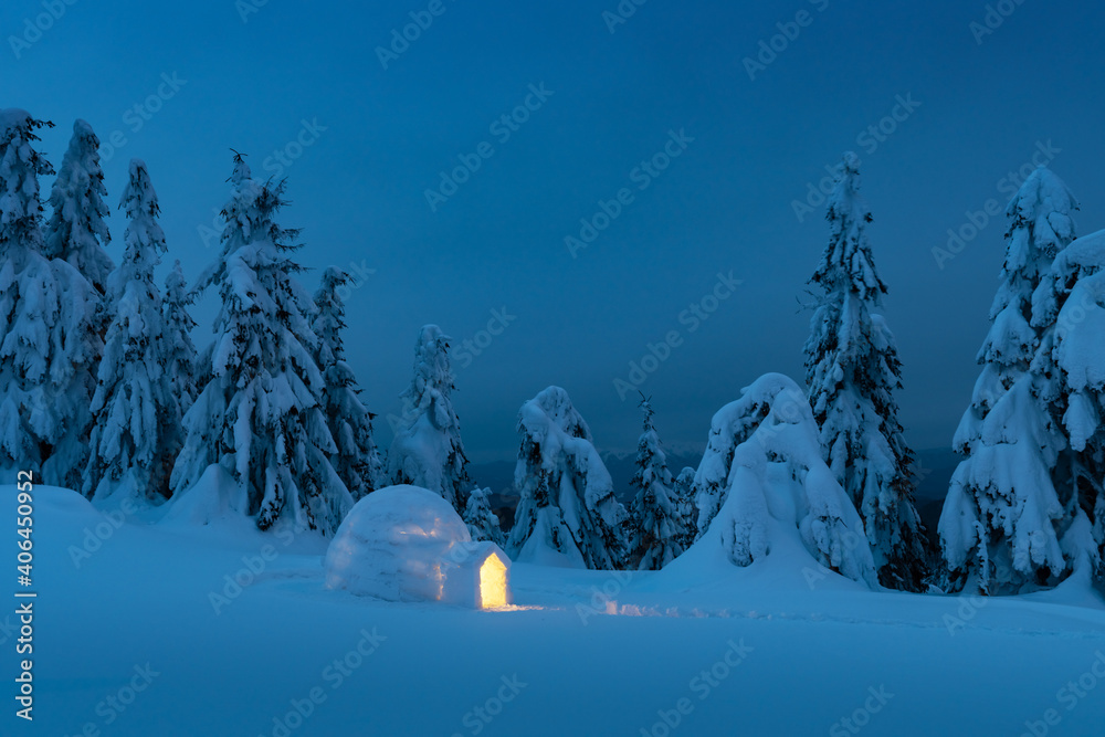 冬季山脉中从内部发光的雪冰屋。傍晚的灯光下白雪覆盖着冷杉