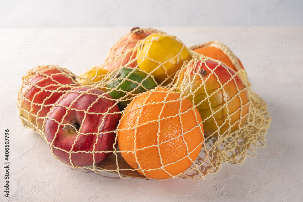 一束混合的有机水果、蔬菜和绿色蔬菜放在浅背景的细袋中。零浪费