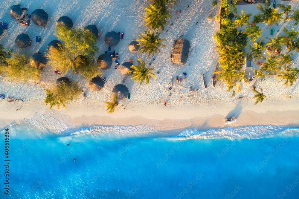 日落时沙滩上的雨伞和绿色棕榈树鸟瞰图。非洲桑给巴尔的暑假
