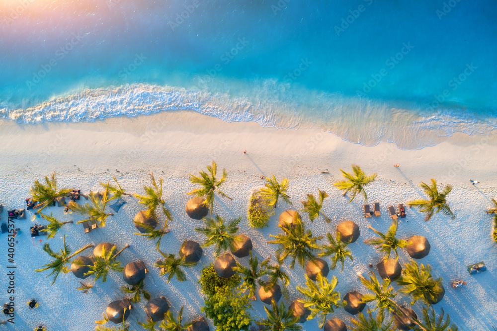 日落时沙滩上的雨伞和绿色棕榈树鸟瞰图。非洲桑给巴尔的暑假