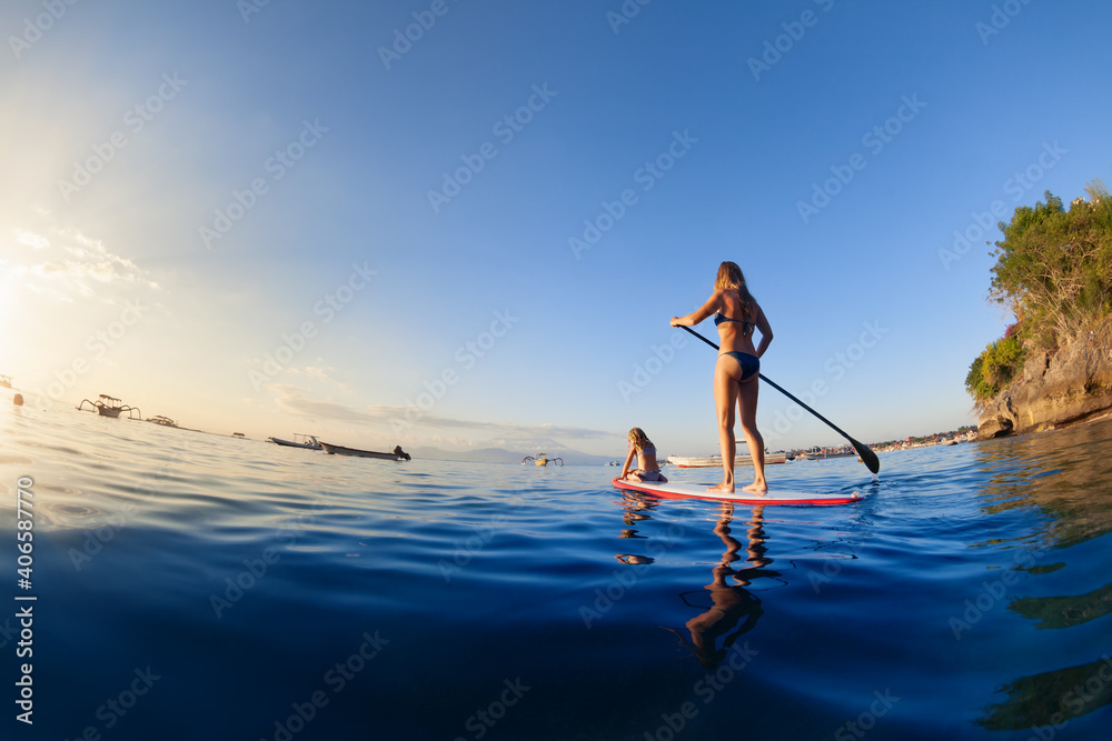 日落海上活跃的桨板冲浪者。年轻的母亲带着小悬崖在立式桨板上划水
