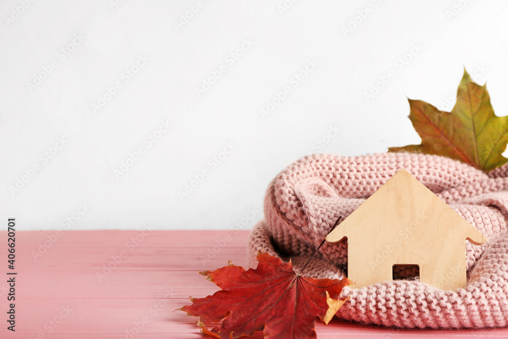 白色背景下的房子、秋叶和桌子上的温暖围巾。供暖概念
