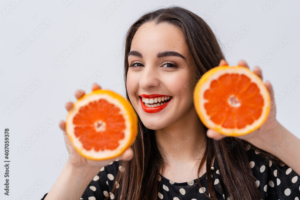 年轻漂亮的女人微笑着，手里拿着白色背景下的橙子片。健康快乐