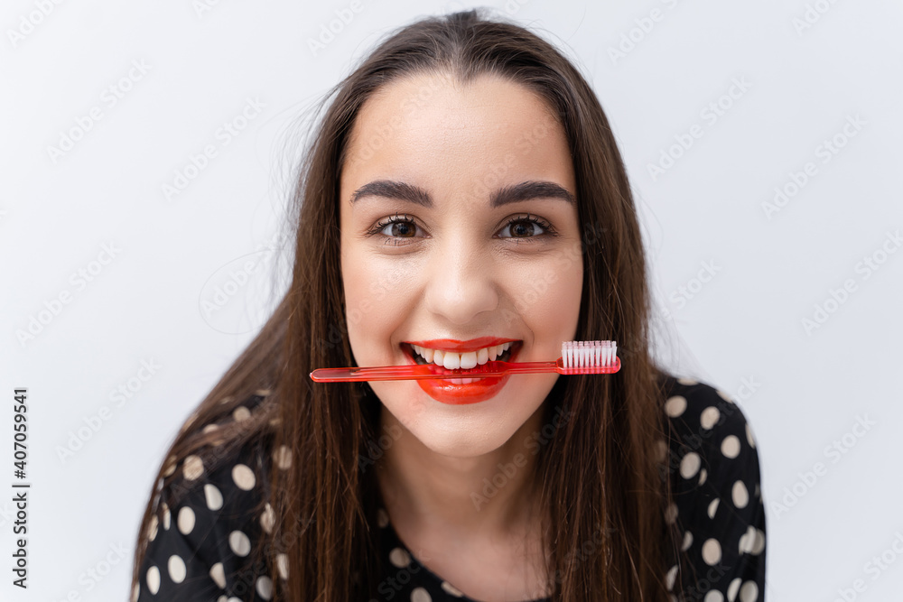 有趣的红唇女孩把牙刷夹在健康的白色牙齿之间。白色背景。口腔护理c