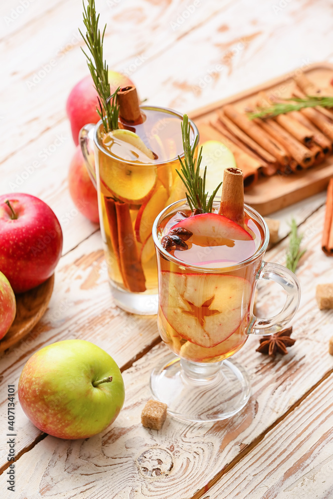 Tasty drink with spices and apple slices in cups on wooden background