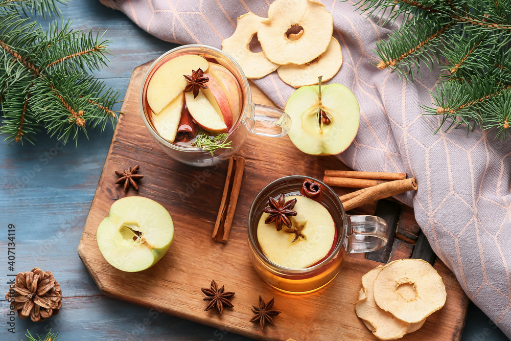 在彩色木质背景下，用杯子装着香料和苹果片的美味饮料