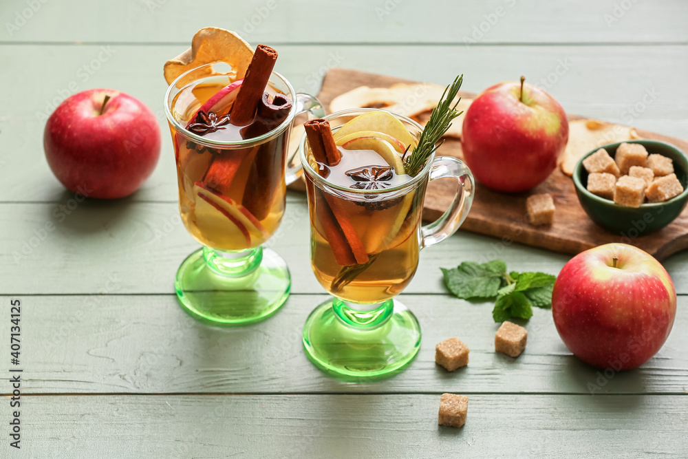 在彩色木质背景下，用杯子装着香料和苹果片的美味饮料