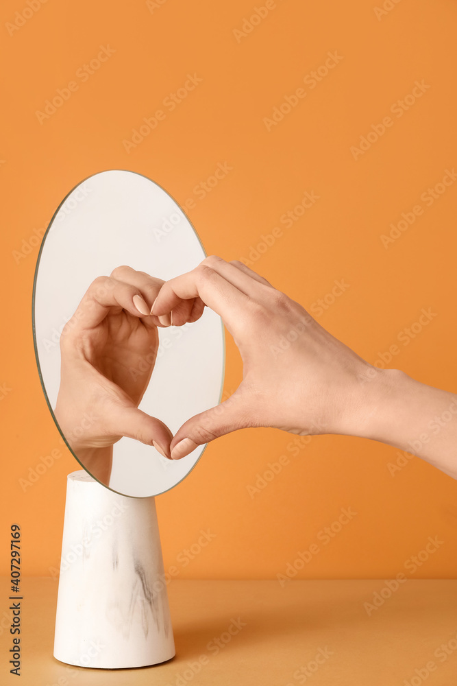 女性的手及其在镜子中的反射在彩色背景下制造心脏