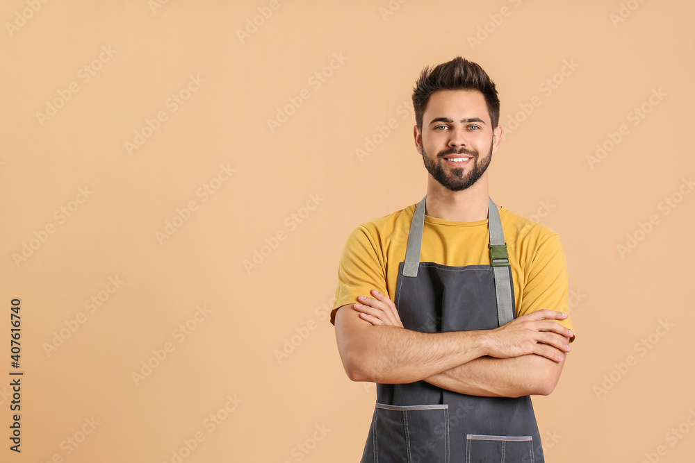 Young man wearing apron on color background