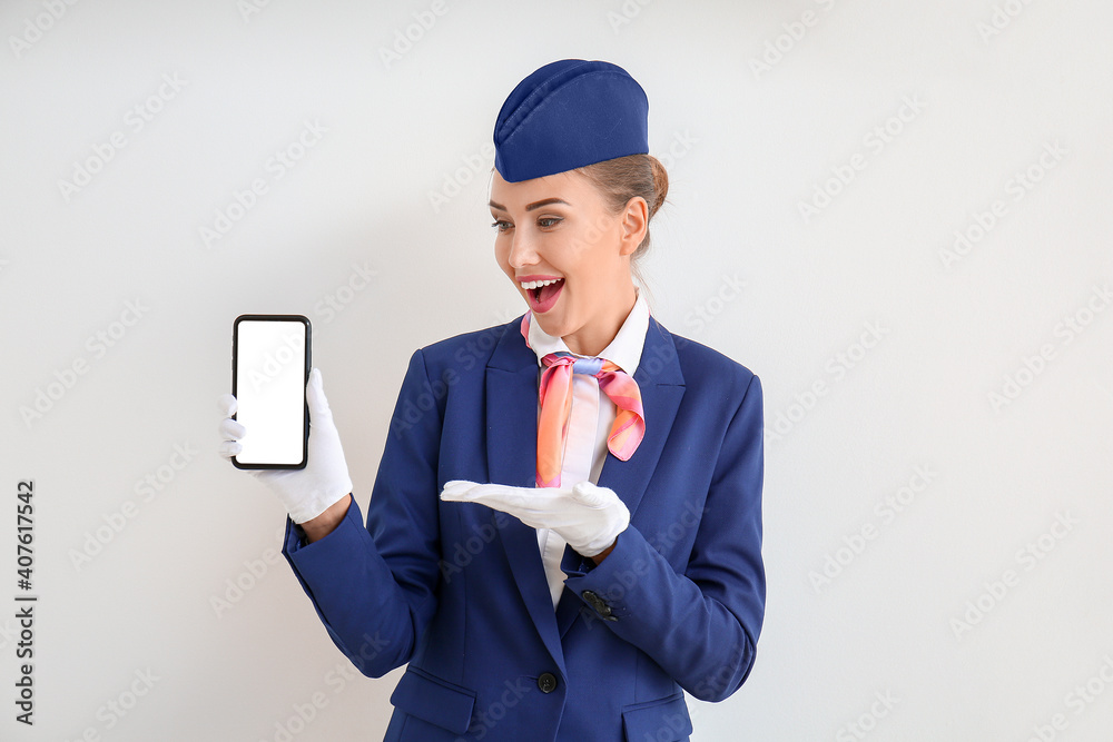 Beautiful stewardess with mobile phone on light background
