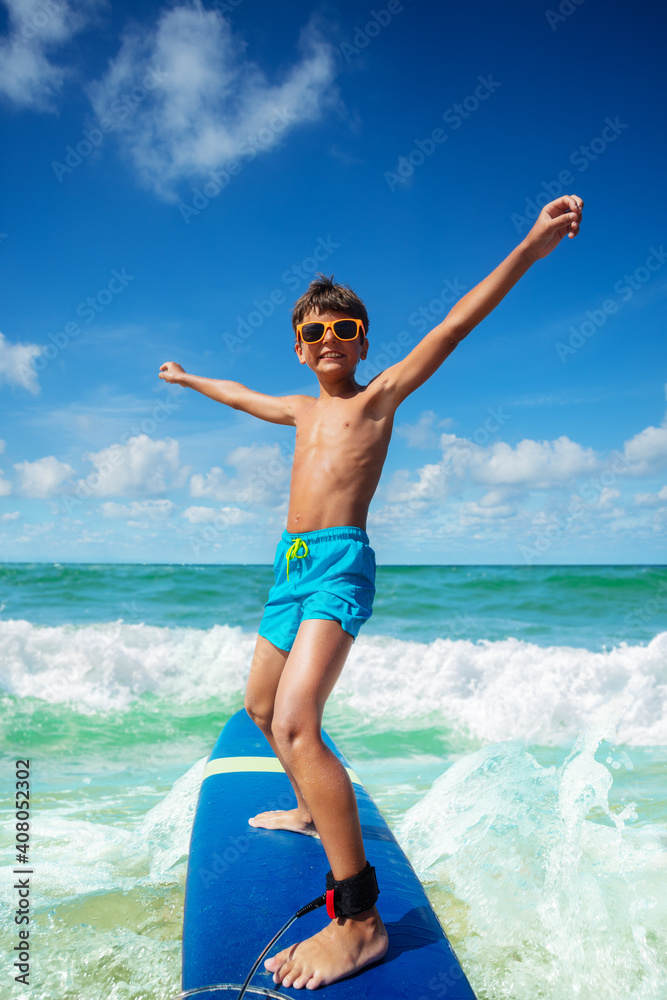 男孩戴着可爱的太阳镜在小海浪上冲浪板练习