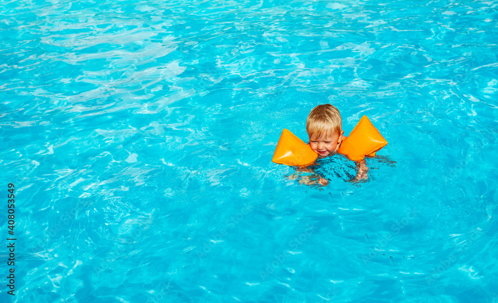 可爱的蹒跚学步的小男孩在游泳池里戴着充气肩带游泳