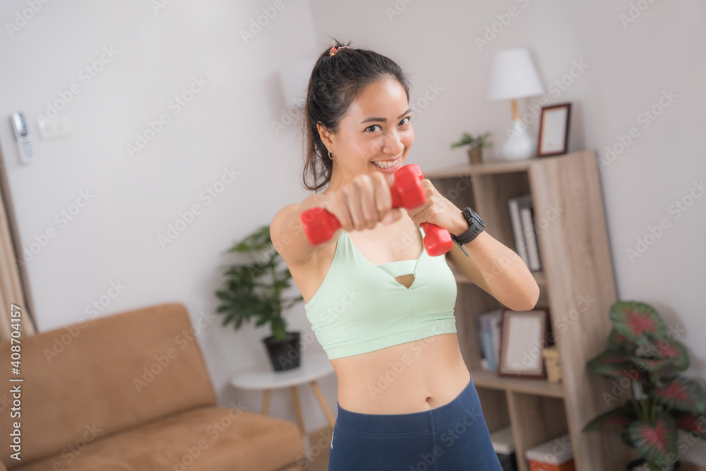 一位亚洲女性在家锻炼，她用一个小哑铃练习拳击。