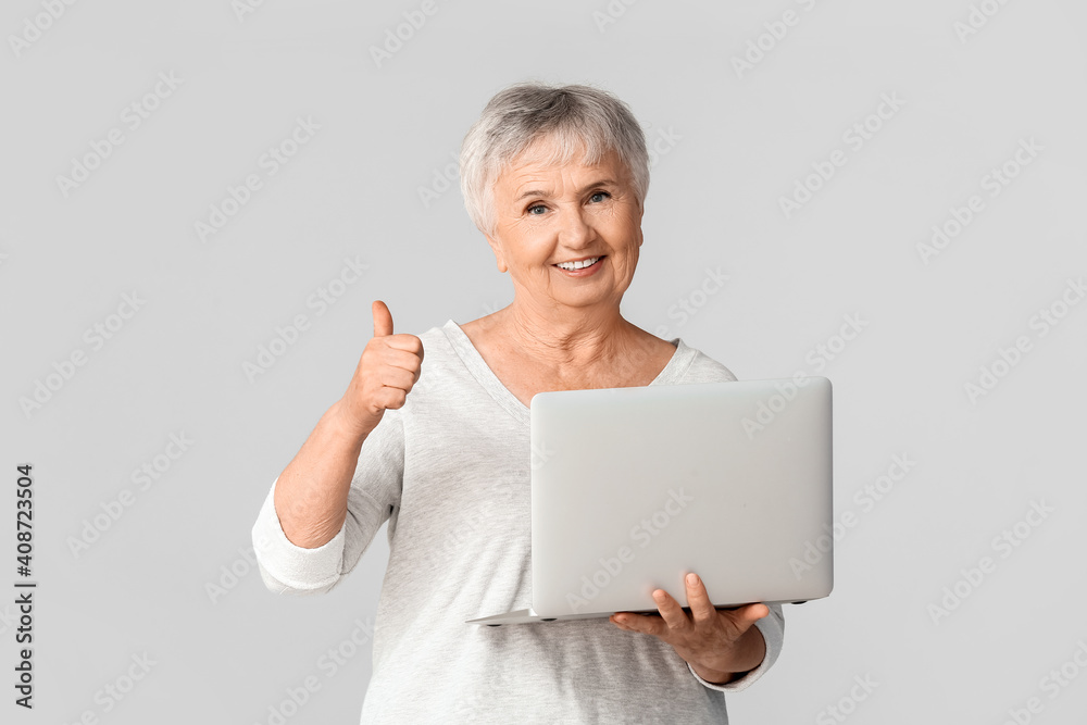 浅色背景下带笔记本电脑的老年妇女