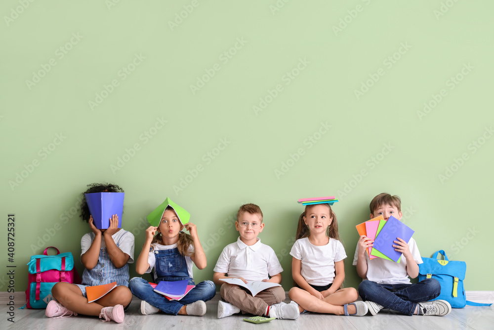 孩子们拿着书坐在彩色背景下的地板上