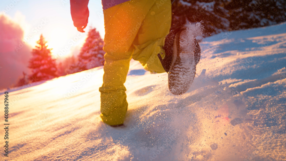 LOW ANGLE: Carefree male tourist runs in the fresh powder snow at sunrise.